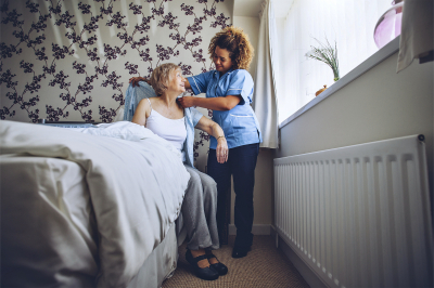 Home Caregiver helping a senior women get dressed in her bedroom